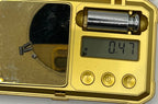 Gold metal detector with digital display showing 0.47, battery compartment, and control buttons.
